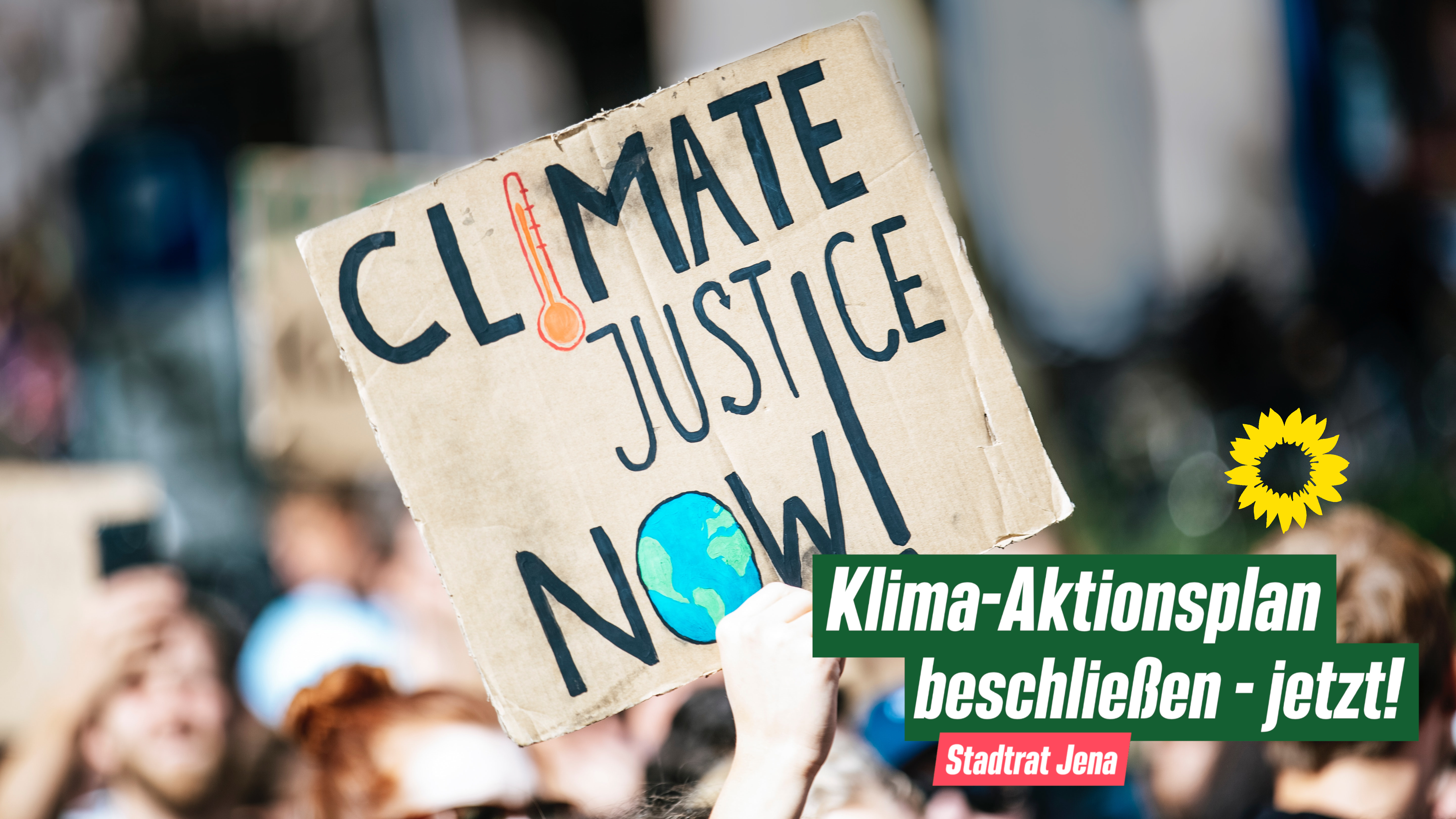Ein Schild wird auf einer Demo hochgehalten, auf dem steht: Climate Justice Now! Im Vordergrund: Klima-Aktionsplan beschließen - jetzt! Darunter: Stadtrat Jena. Daneben: Parteilogo der Grünen.